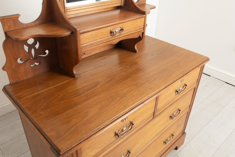 An Arts and Crafts walnut dressing chest featuring two short over two long drawers, a mirror superstructure, and decorative pierced cut-outs. View III