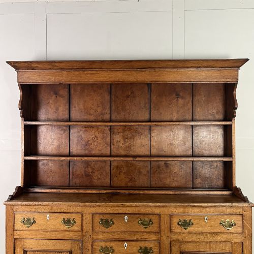 fig 2. An early nineteenth-century oak kitchen dresser featuring an open upper plate rack over a base with central drawers and side cupboard doors with brass hardware.
