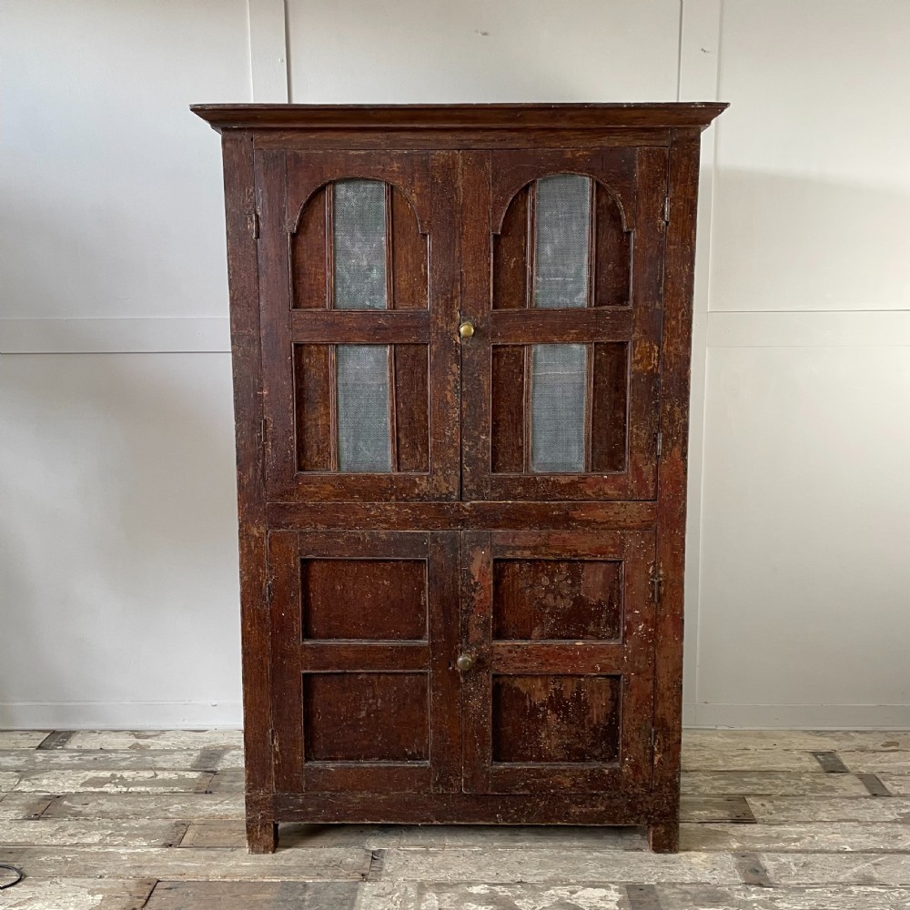 A late 18th-century dark brown painted pine food cupboard with arched mesh upper doors and fielded panel lower doors.
