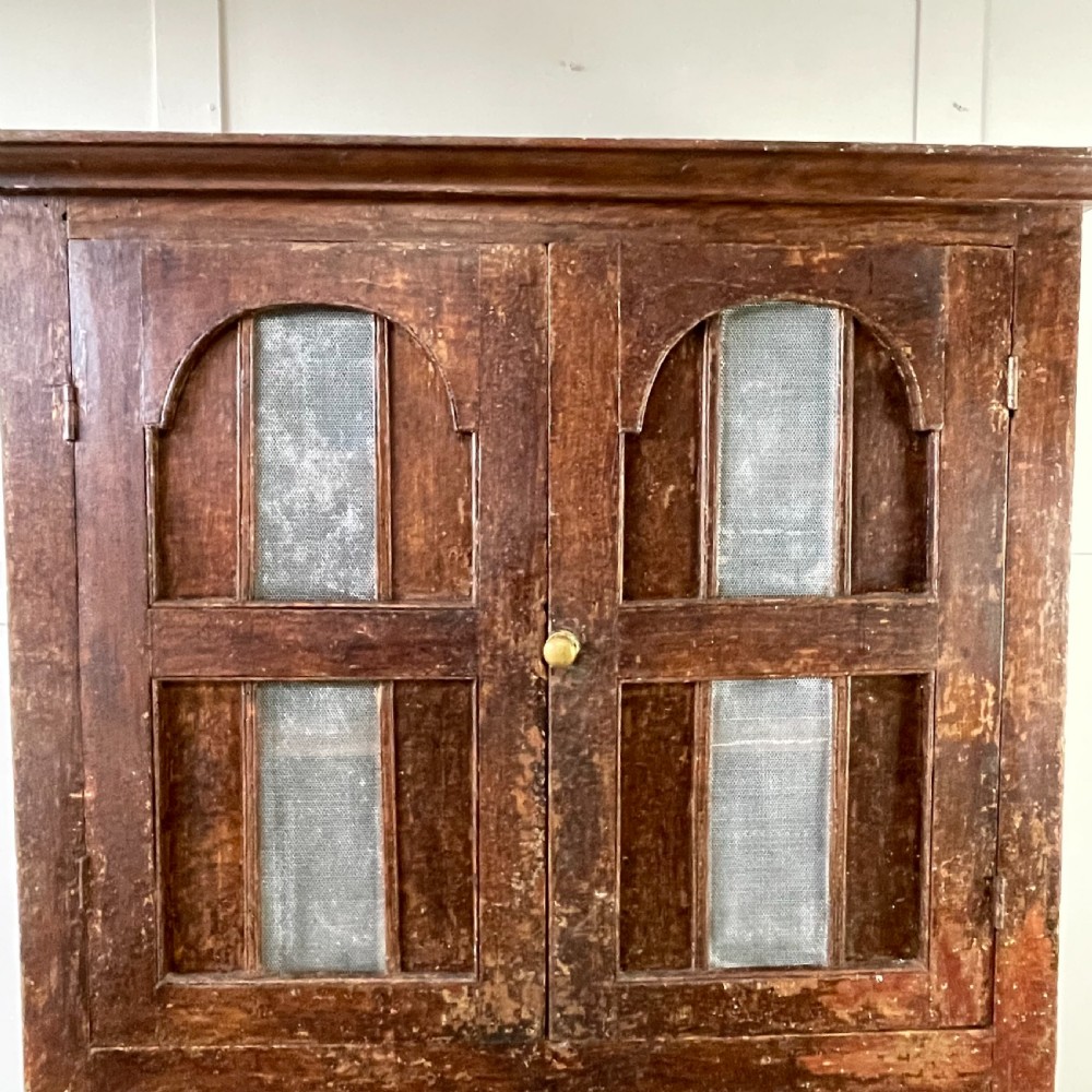 A late 18th-century dark brown painted pine food cupboard with arched mesh upper doors and fielded panel lower doors. View VII
