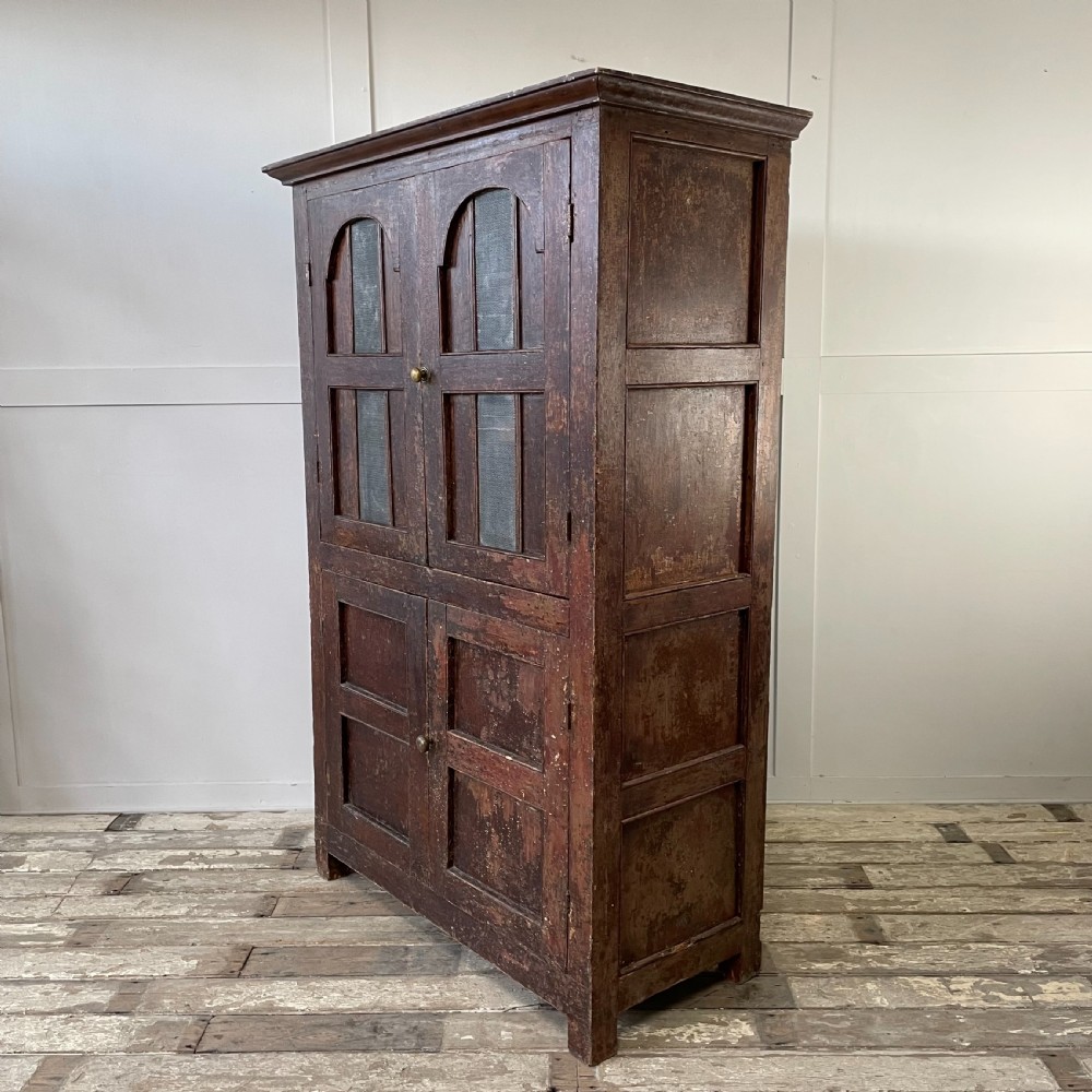 A late 18th-century dark brown painted pine food cupboard with arched mesh upper doors and fielded panel lower doors. View XII