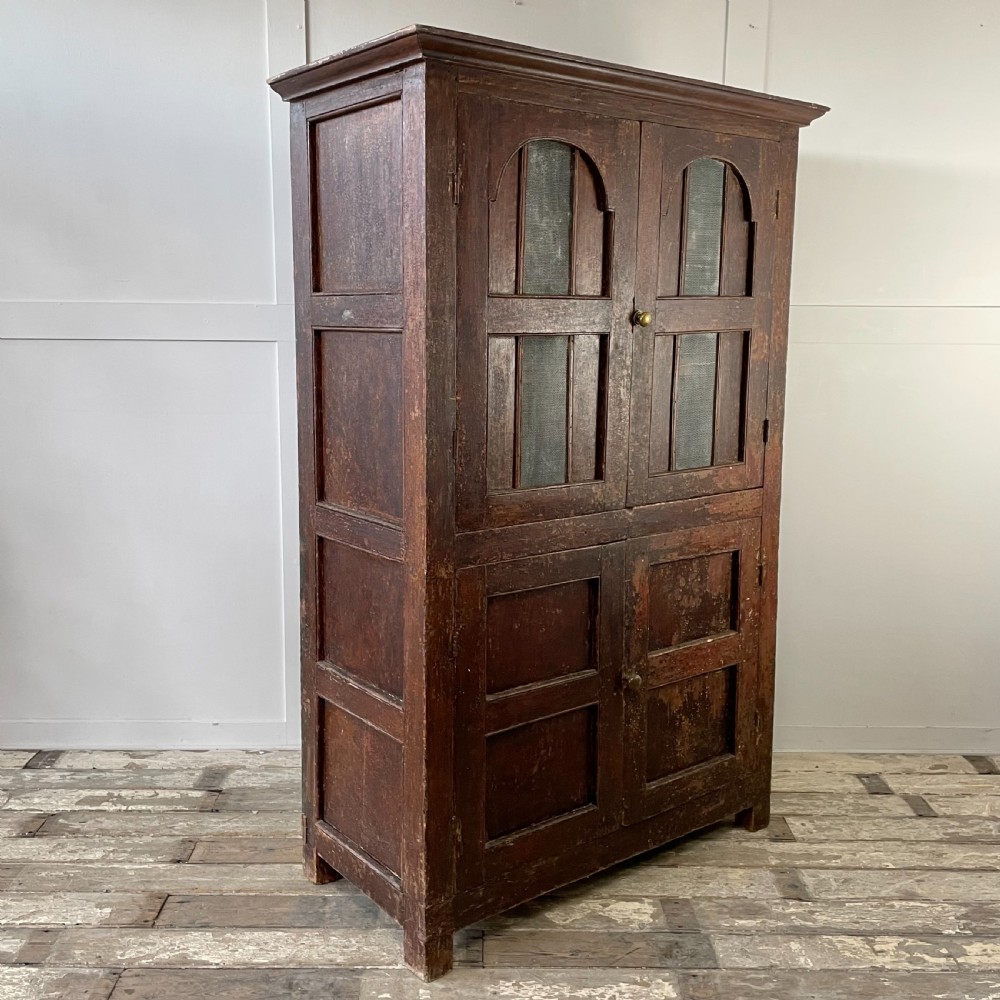 A late 18th-century dark brown painted pine food cupboard with arched mesh upper doors and fielded panel lower doors. View XIII