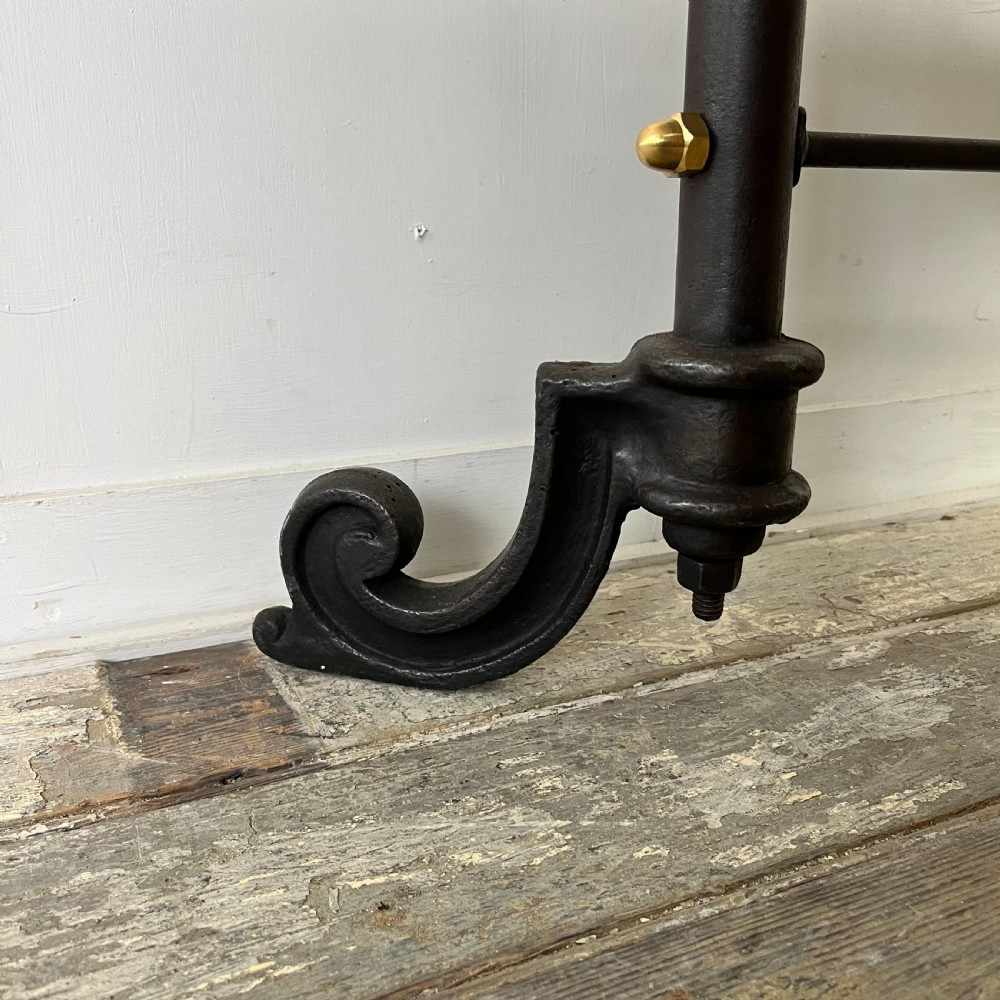A tall Victorian-style black metal frame display stand featuring three timber slatted shelves, decorative brass finials at the top corners, and scrolled foot supports. View IV