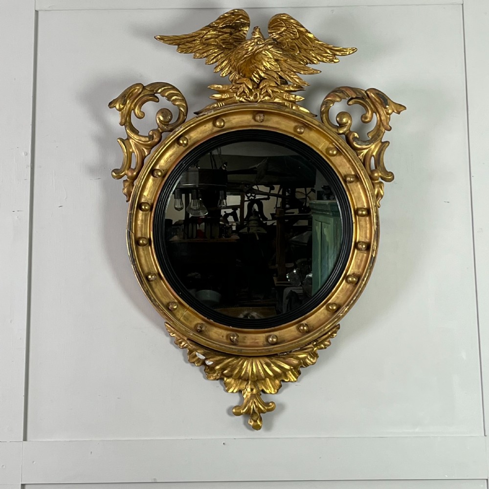 A circular carved giltwood convex wall mirror surmounted by a carved eagle crest with spread wings and an acanthus leaf apron.