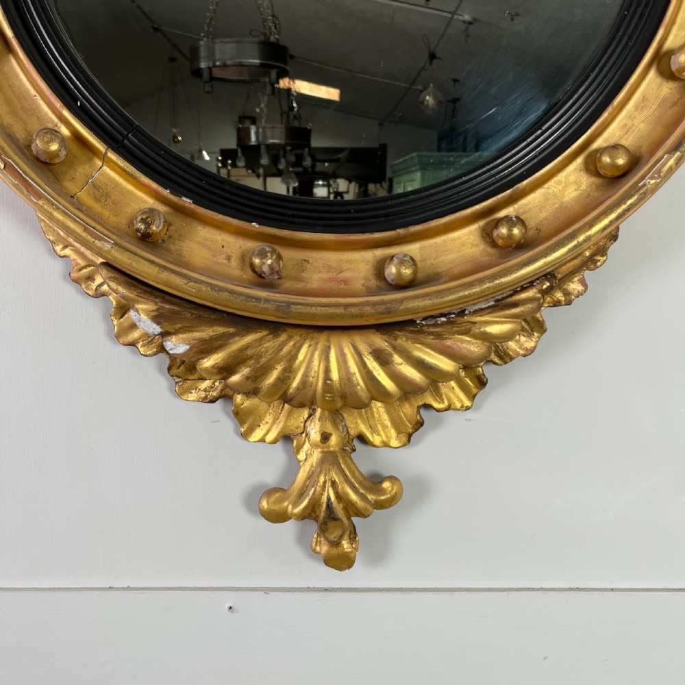 A circular carved giltwood convex wall mirror surmounted by a carved eagle crest with spread wings and an acanthus leaf apron. View II
