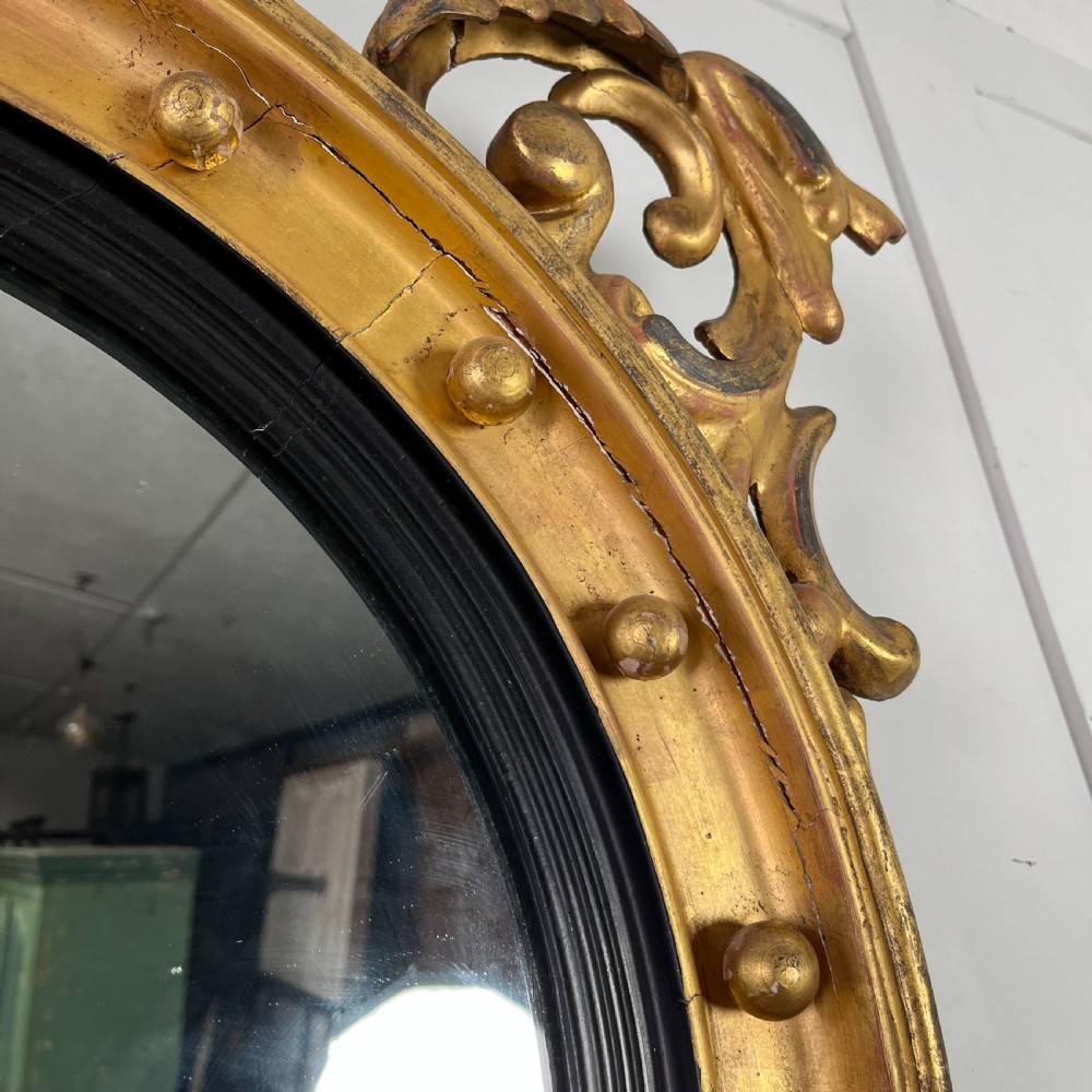 A circular carved giltwood convex wall mirror surmounted by a carved eagle crest with spread wings and an acanthus leaf apron. View V