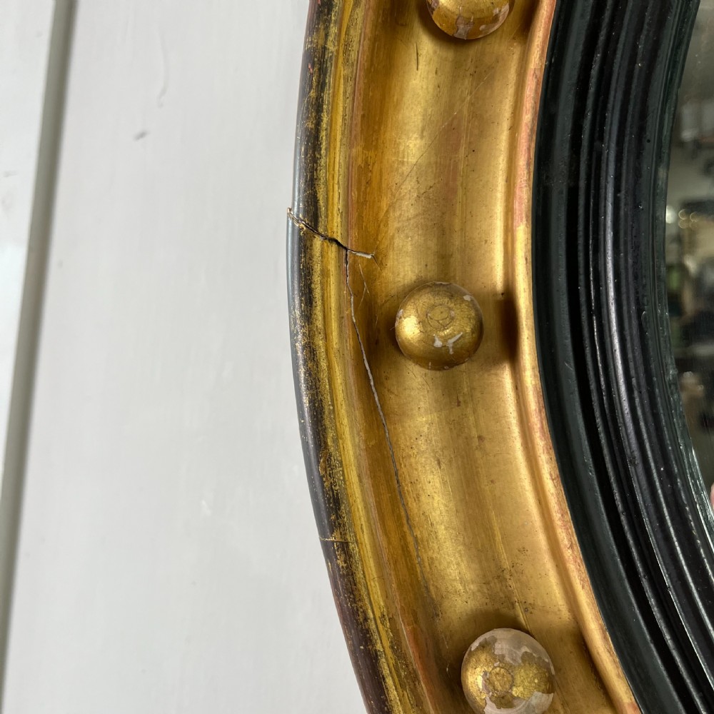 A circular carved giltwood convex wall mirror surmounted by a carved eagle crest with spread wings and an acanthus leaf apron. View VI