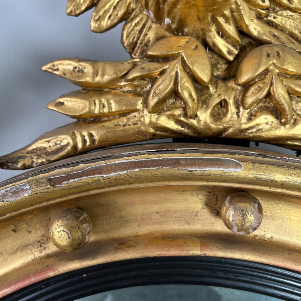 A circular carved giltwood convex wall mirror surmounted by a carved eagle crest with spread wings and an acanthus leaf apron. View VII