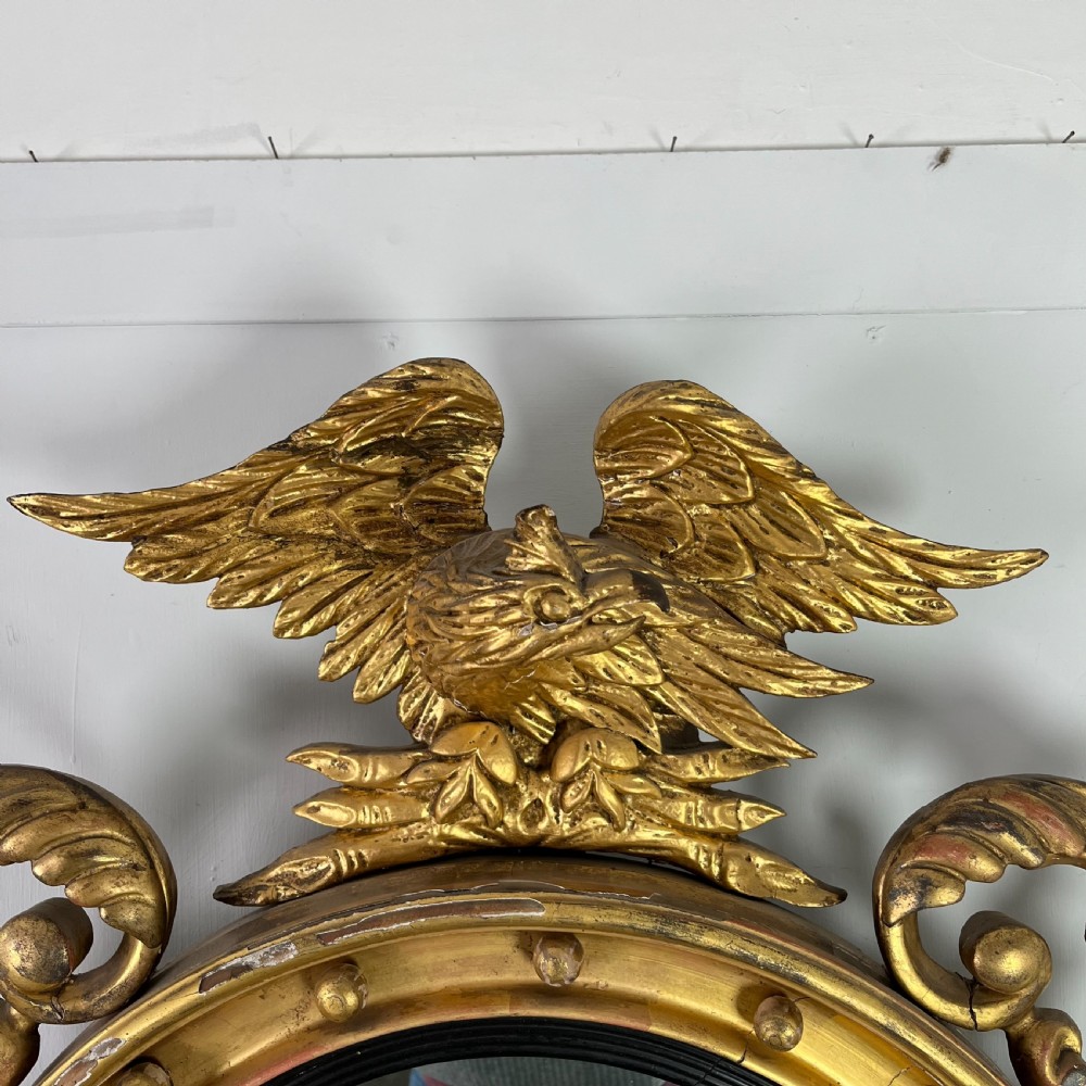 A circular carved giltwood convex wall mirror surmounted by a carved eagle crest with spread wings and an acanthus leaf apron. View XIV