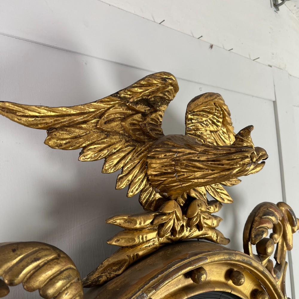 A circular carved giltwood convex wall mirror surmounted by a carved eagle crest with spread wings and an acanthus leaf apron. View XV