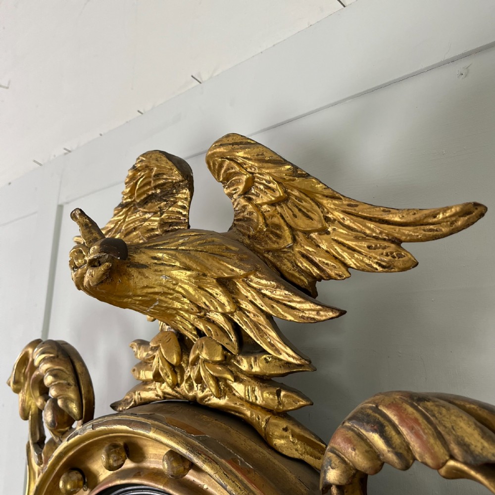 A circular carved giltwood convex wall mirror surmounted by a carved eagle crest with spread wings and an acanthus leaf apron. View XVII