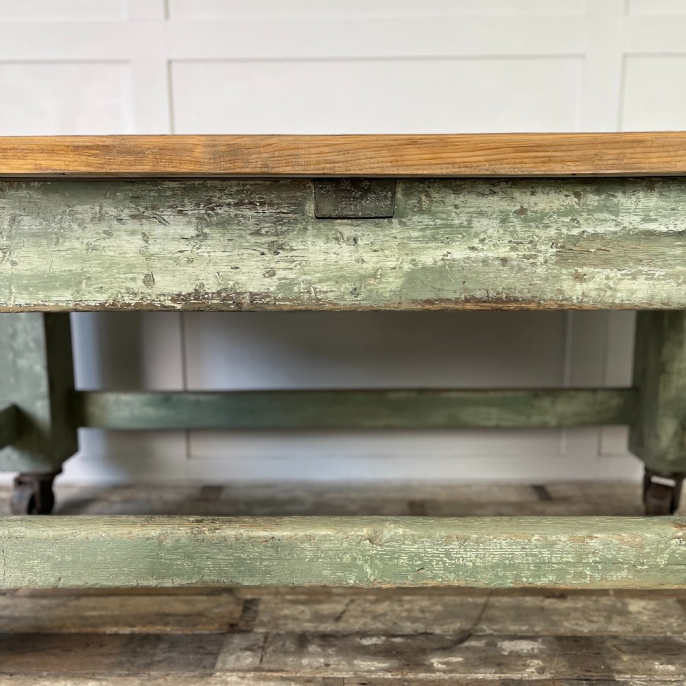 An early 20th-century pine work table featuring a natural scrubbed wood top and a distressed sage green painted frame supported by heavy cast iron castors. View VII