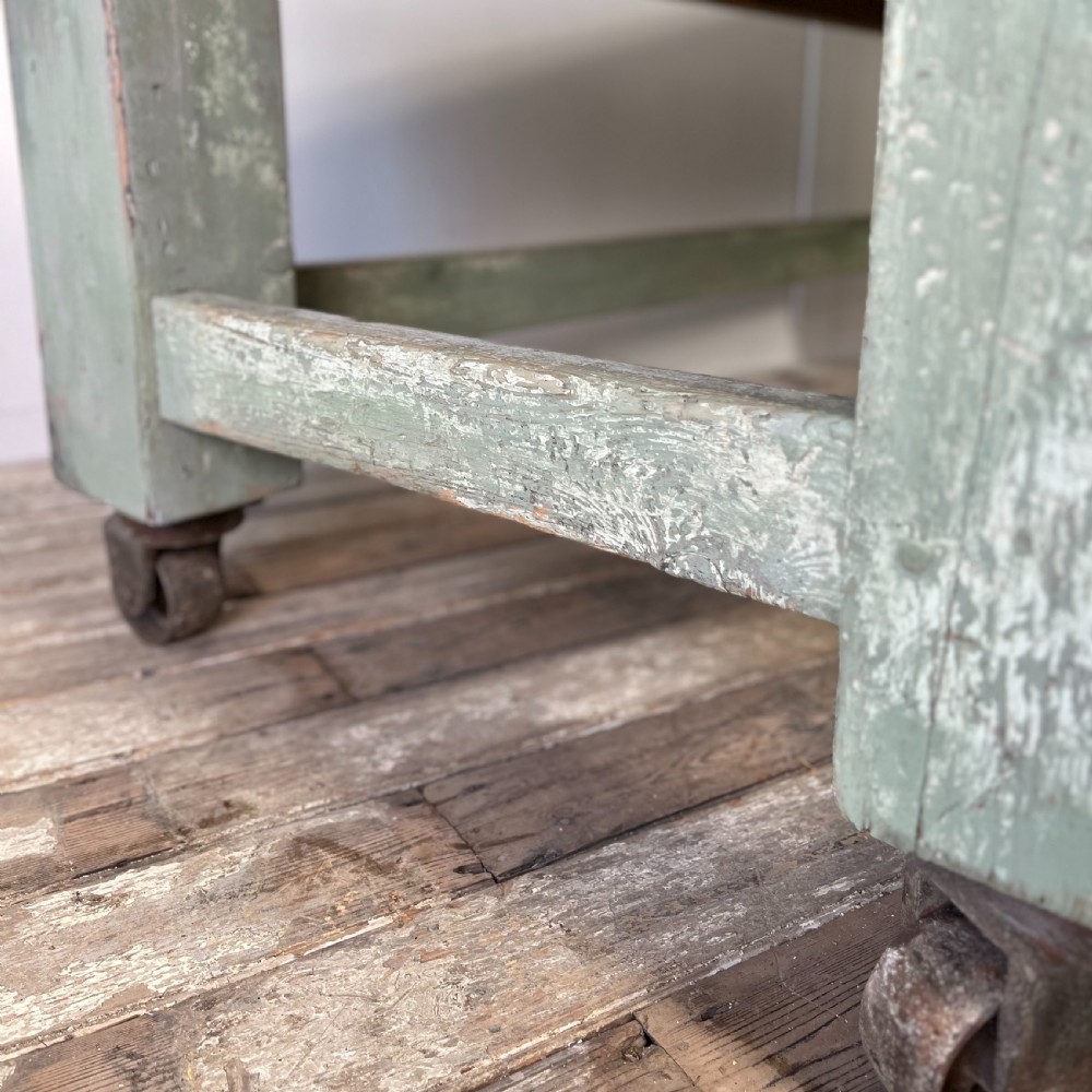 An early 20th-century pine work table featuring a natural scrubbed wood top and a distressed sage green painted frame supported by heavy cast iron castors. View VIII