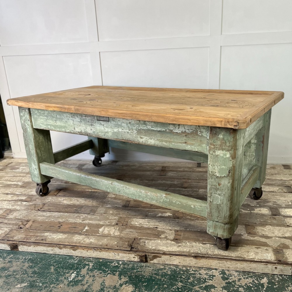 An early 20th-century pine work table featuring a natural scrubbed wood top and a distressed sage green painted frame supported by heavy cast iron castors. View IX