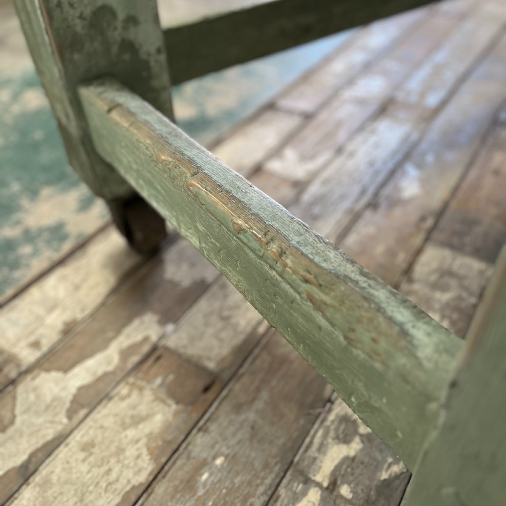 An early 20th-century pine work table featuring a natural scrubbed wood top and a distressed sage green painted frame supported by heavy cast iron castors. View X