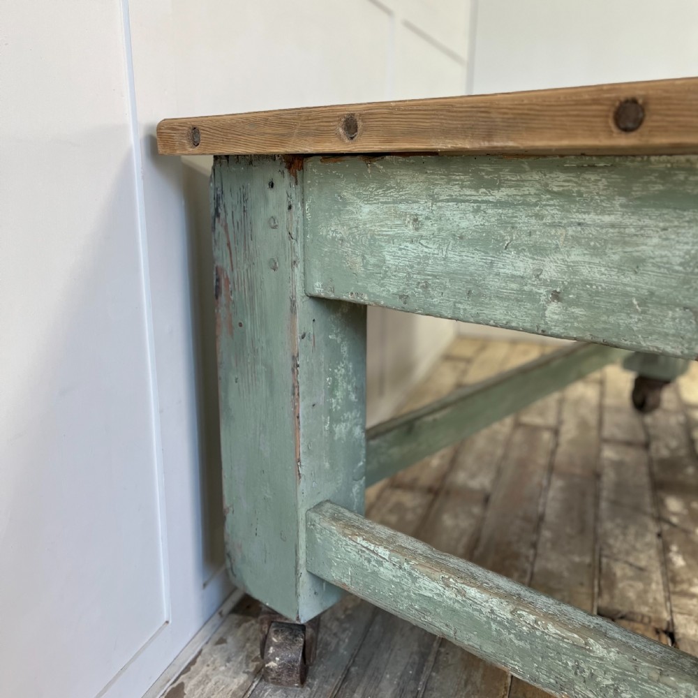An early 20th-century pine work table featuring a natural scrubbed wood top and a distressed sage green painted frame supported by heavy cast iron castors. View XI