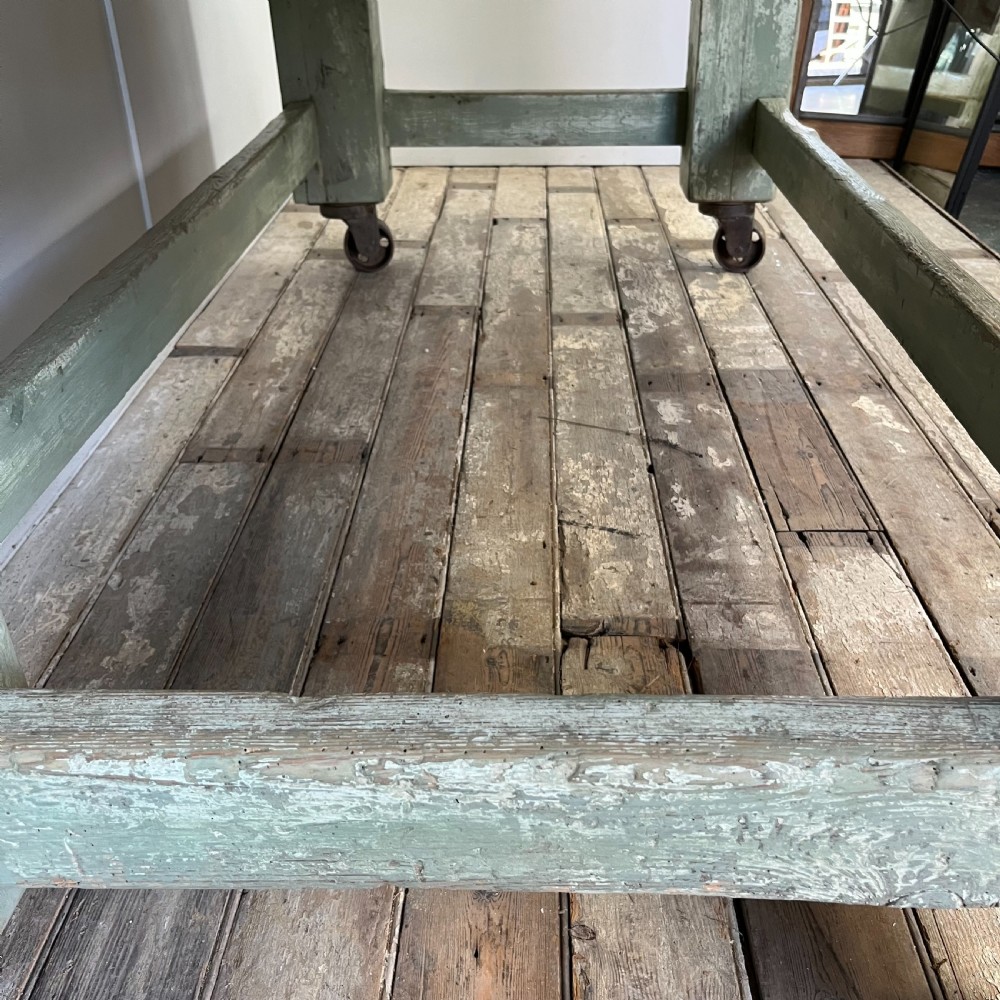 An early 20th-century pine work table featuring a natural scrubbed wood top and a distressed sage green painted frame supported by heavy cast iron castors. View XII