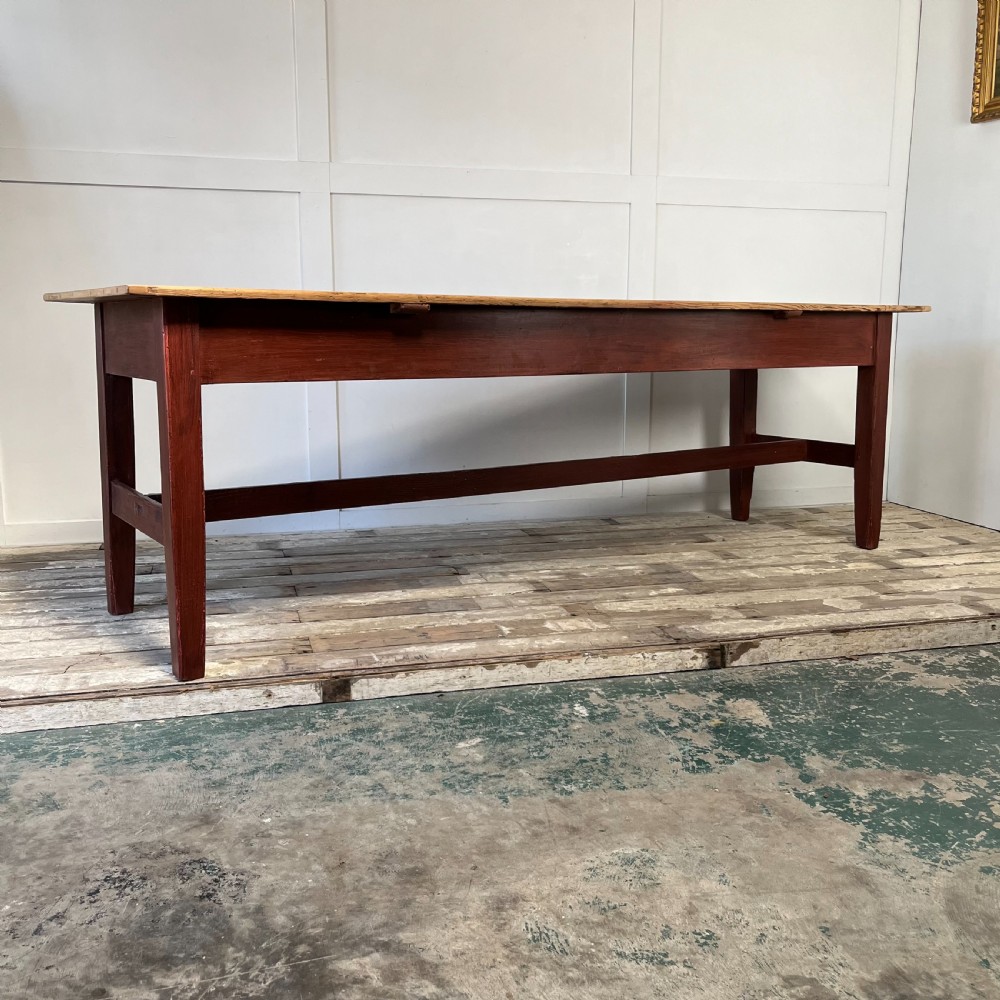 A long 19th-century Welsh pine refectory table featuring a natural timber plank top supported by a dark red painted frame with lower stretchers.