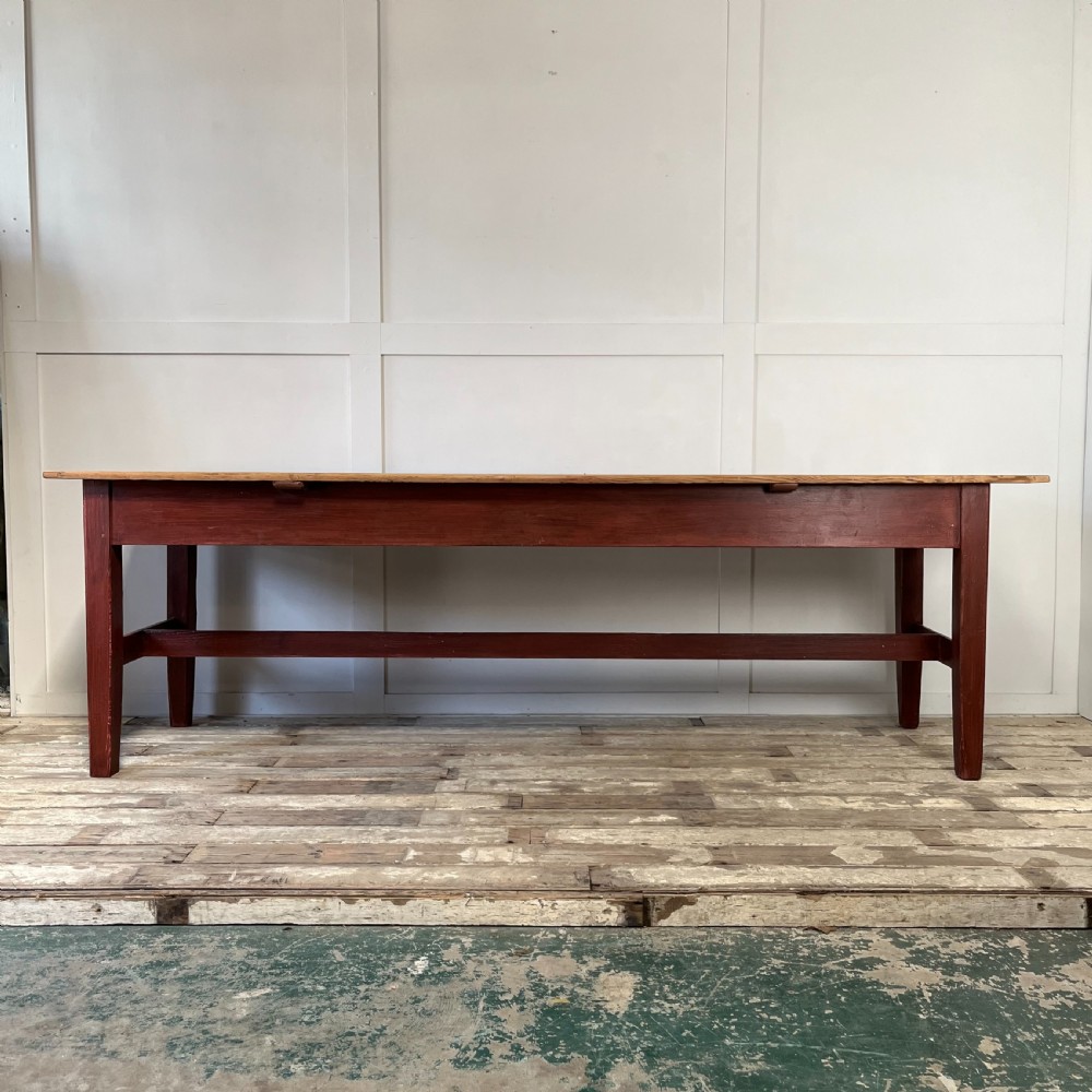 A long 19th-century Welsh pine refectory table featuring a natural timber plank top supported by a dark red painted frame with lower stretchers. View II