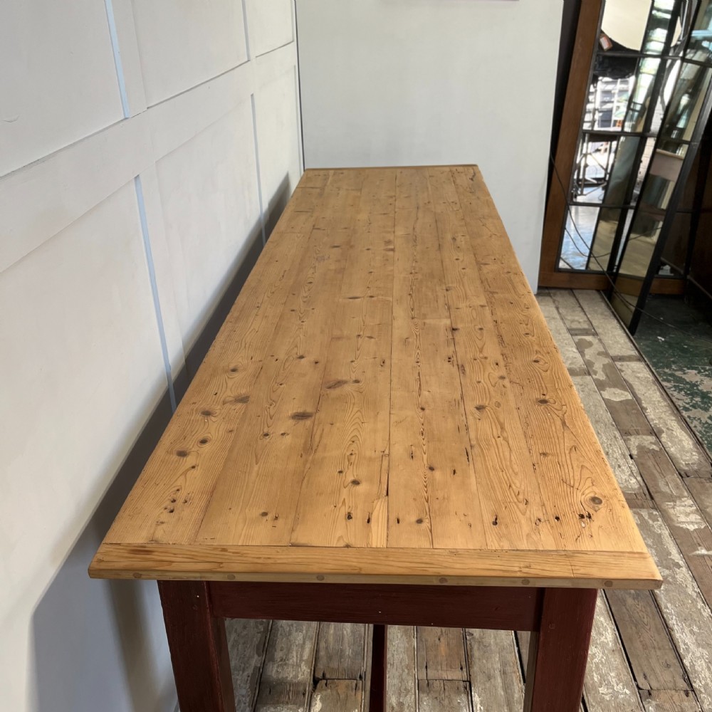 A long 19th-century Welsh pine refectory table featuring a natural timber plank top supported by a dark red painted frame with lower stretchers. View XII
