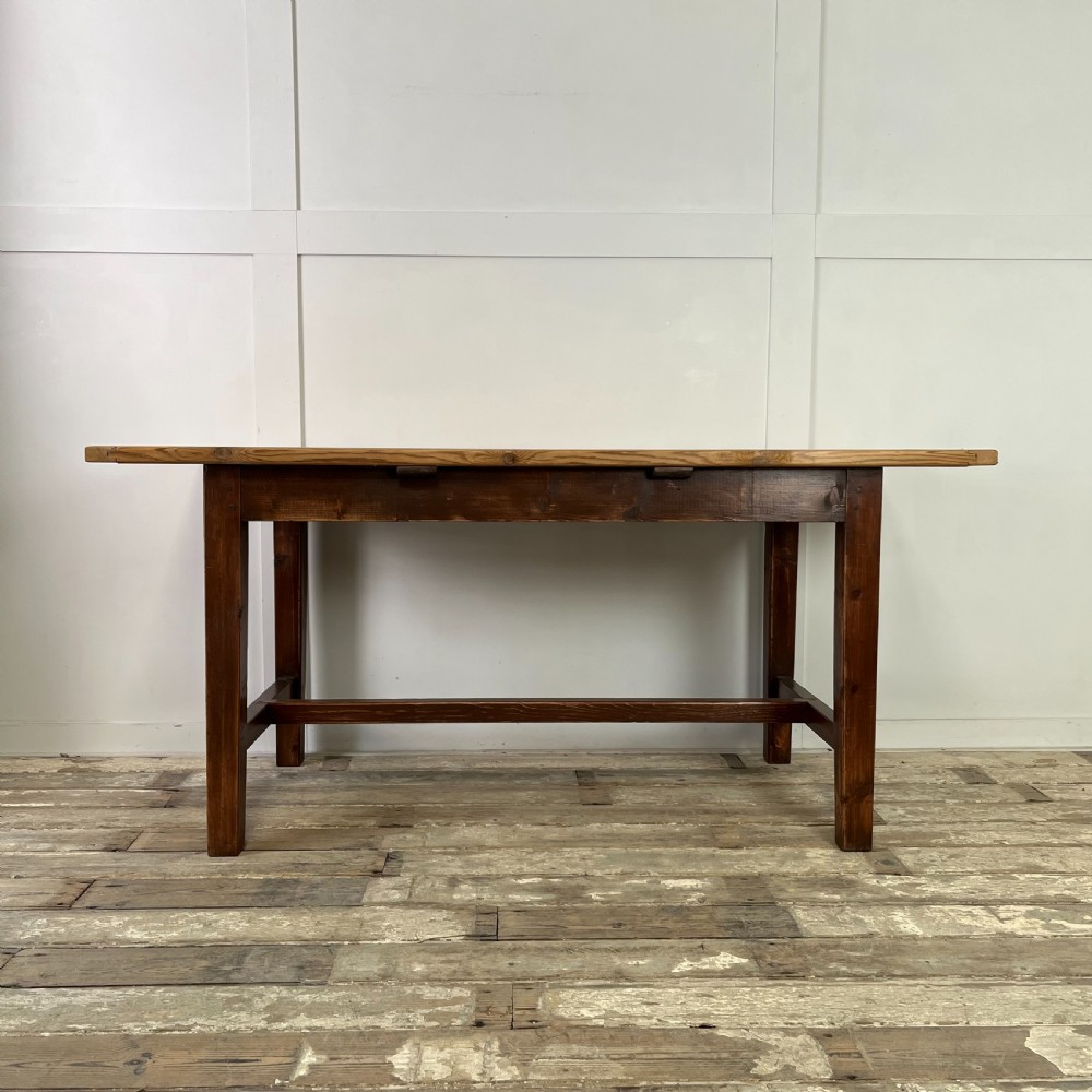 A 19th-century Welsh pine kitchen table featuring a light wood plank top supported by a dark stained wooden frame with square legs and a low stretcher.