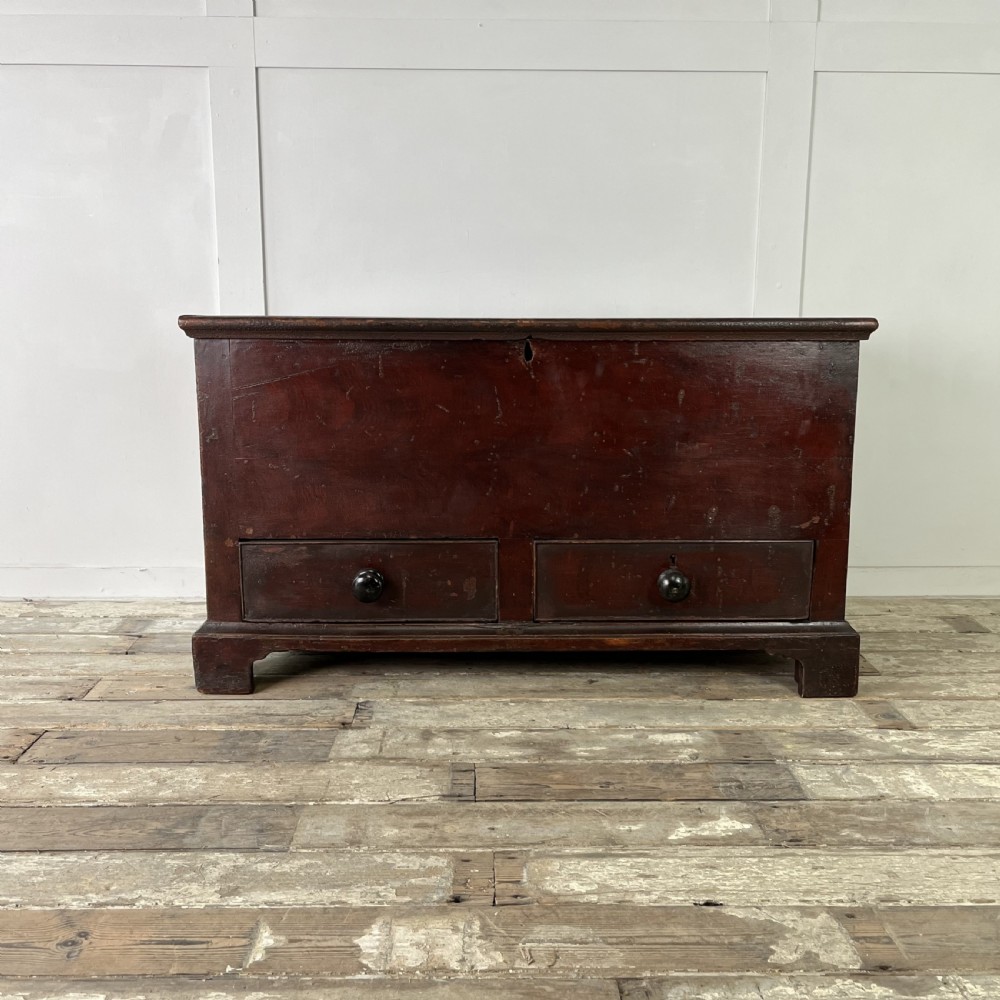 A dark red painted Georgian pine mule chest featuring a hinged top lid above two lower drawers with turned wooden knobs.