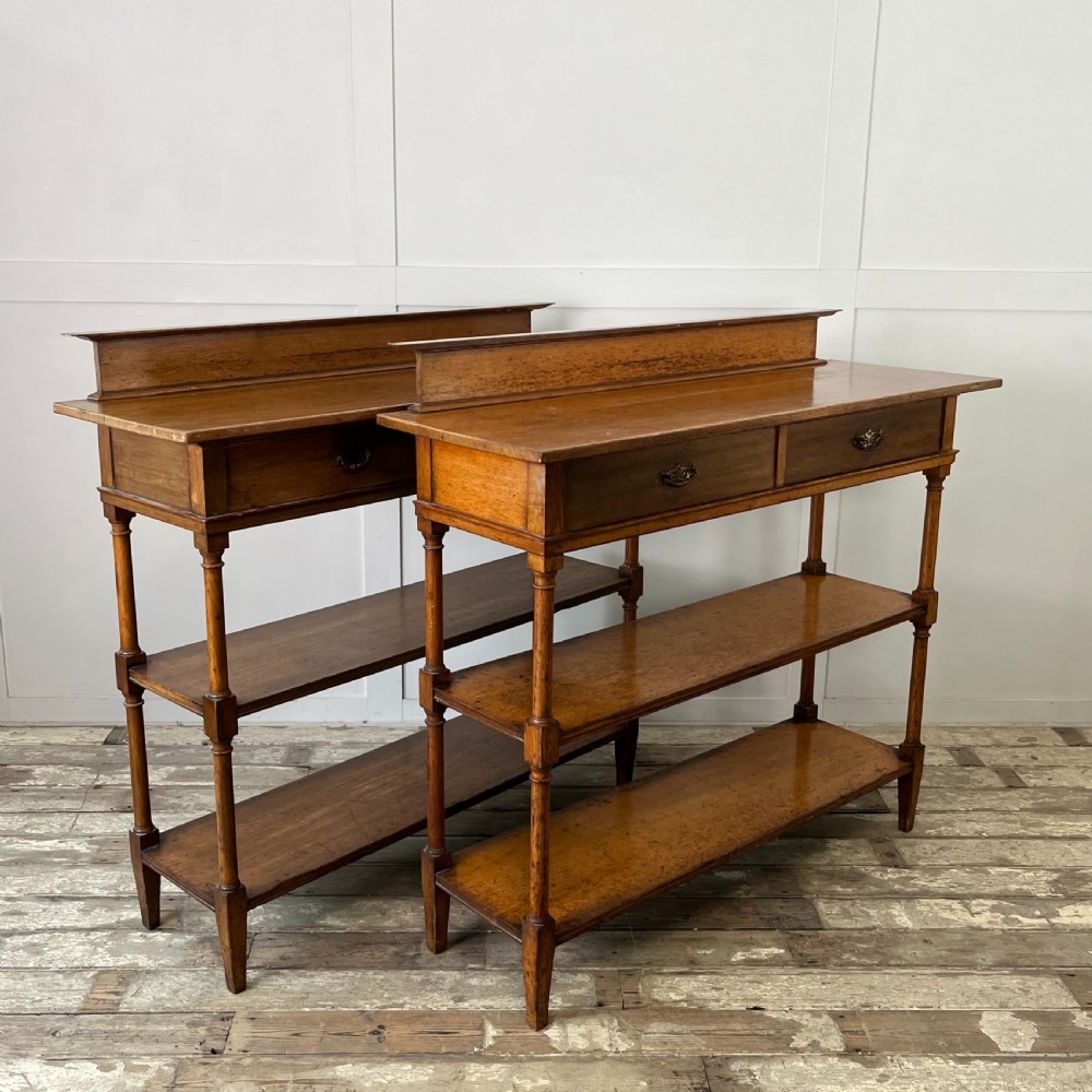 A pair of Victorian oak serving tables featuring tiered shelves, turned upright supports, and two frieze drawers with brass handles.