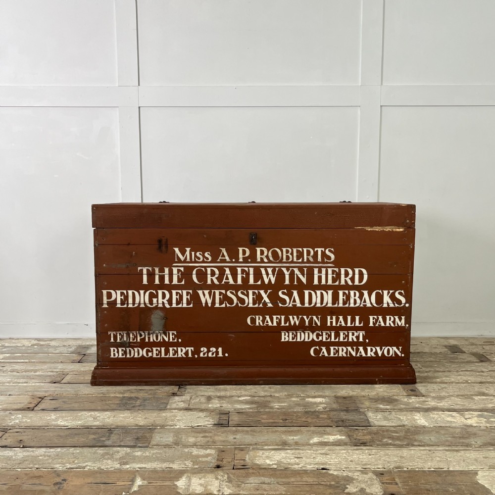 A rectangular reddish-brown painted pine storage chest featuring white hand-painted agricultural typography on the front panel.