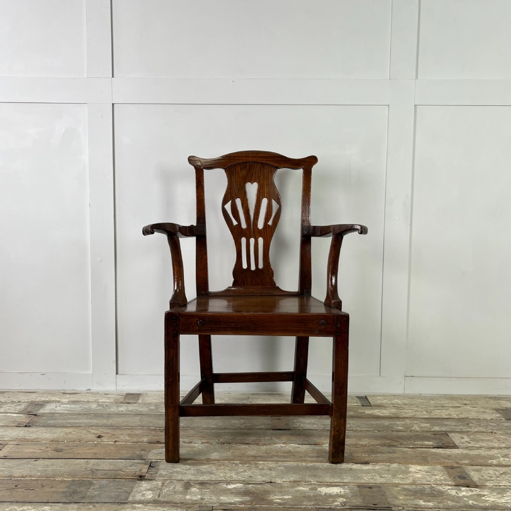 A dark brown early nineteenth-century elm armchair featuring a shaped top rail, a pierced vertical back splat, curved armrests, a solid timber seat, and straight legs joined by stretchers.
