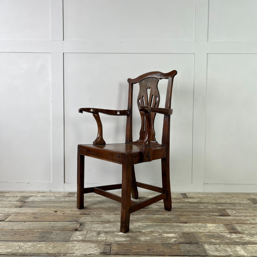 A dark brown early nineteenth-century elm armchair featuring a shaped top rail, a pierced vertical back splat, curved armrests, a solid timber seat, and straight legs joined by stretchers. View II