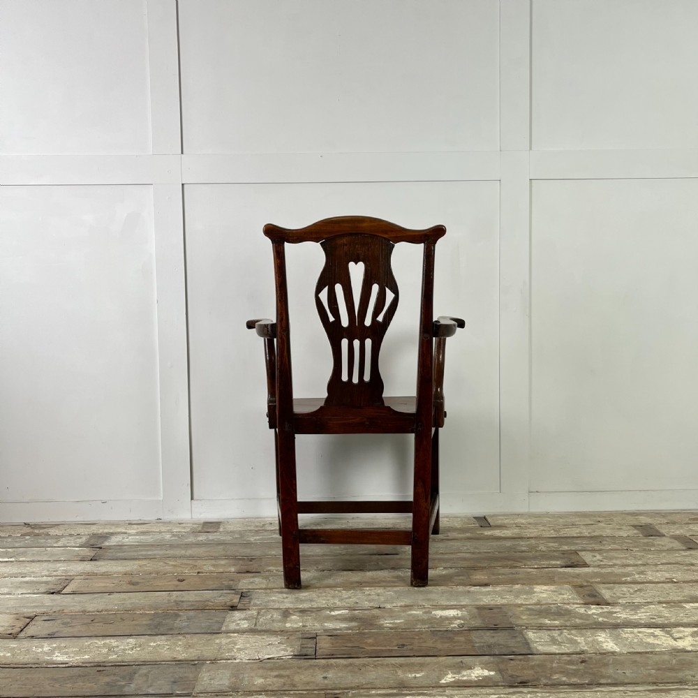 A dark brown early nineteenth-century elm armchair featuring a shaped top rail, a pierced vertical back splat, curved armrests, a solid timber seat, and straight legs joined by stretchers. View V