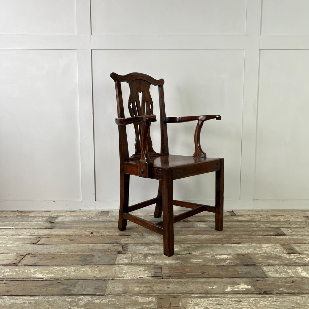 A dark brown early nineteenth-century elm armchair featuring a shaped top rail, a pierced vertical back splat, curved armrests, a solid timber seat, and straight legs joined by stretchers. View VII