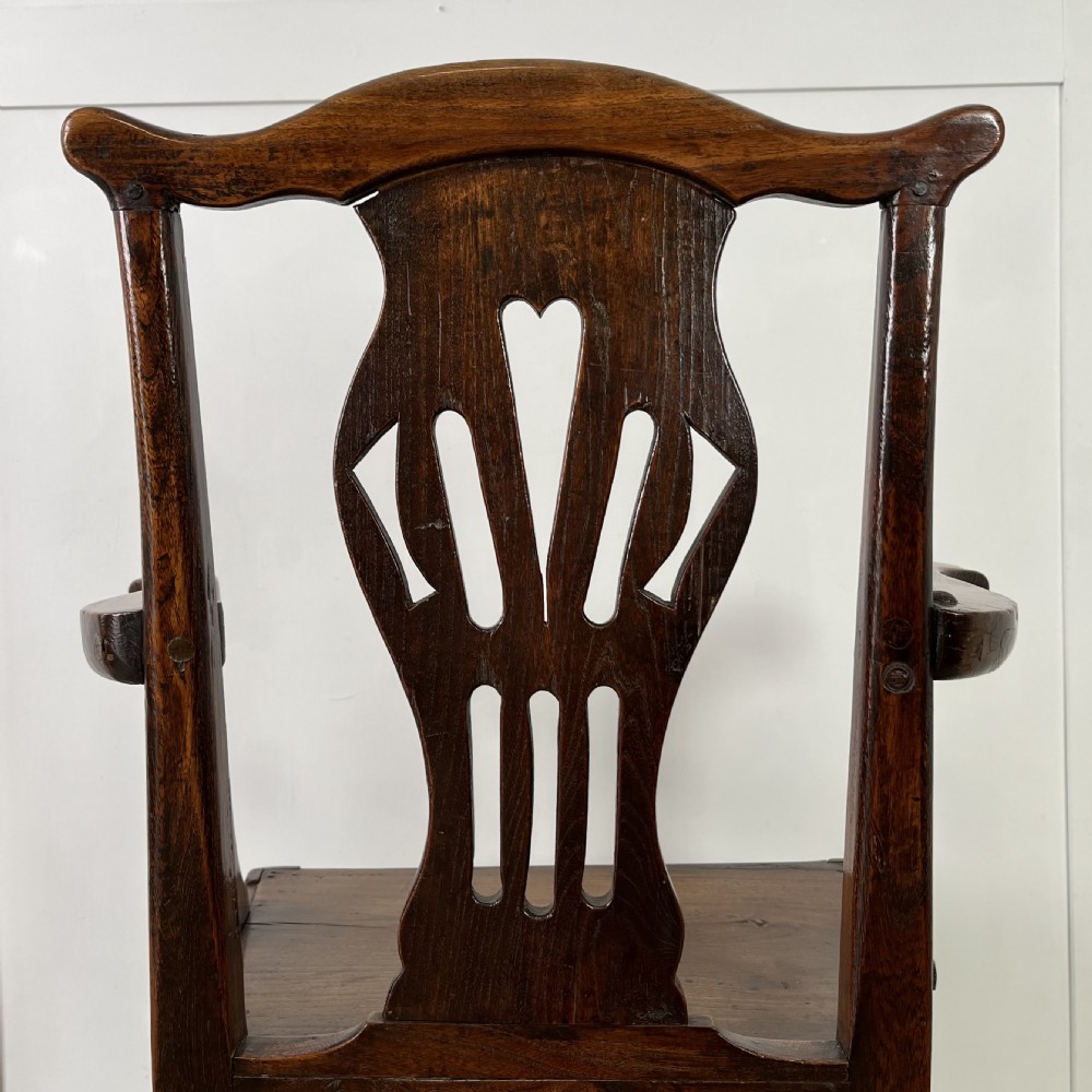 A dark brown early nineteenth-century elm armchair featuring a shaped top rail, a pierced vertical back splat, curved armrests, a solid timber seat, and straight legs joined by stretchers. View IX