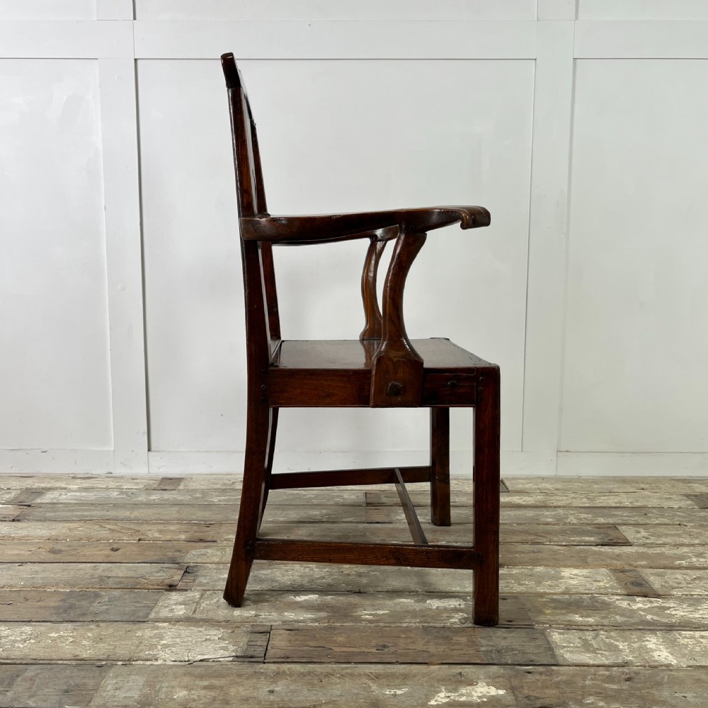 A dark brown early nineteenth-century elm armchair featuring a shaped top rail, a pierced vertical back splat, curved armrests, a solid timber seat, and straight legs joined by stretchers. View XVIII