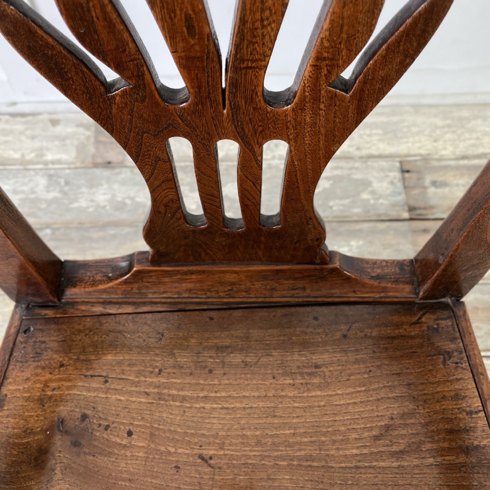 A dark brown early nineteenth-century elm armchair featuring a shaped top rail, a pierced vertical back splat, curved armrests, a solid timber seat, and straight legs joined by stretchers. View XIX