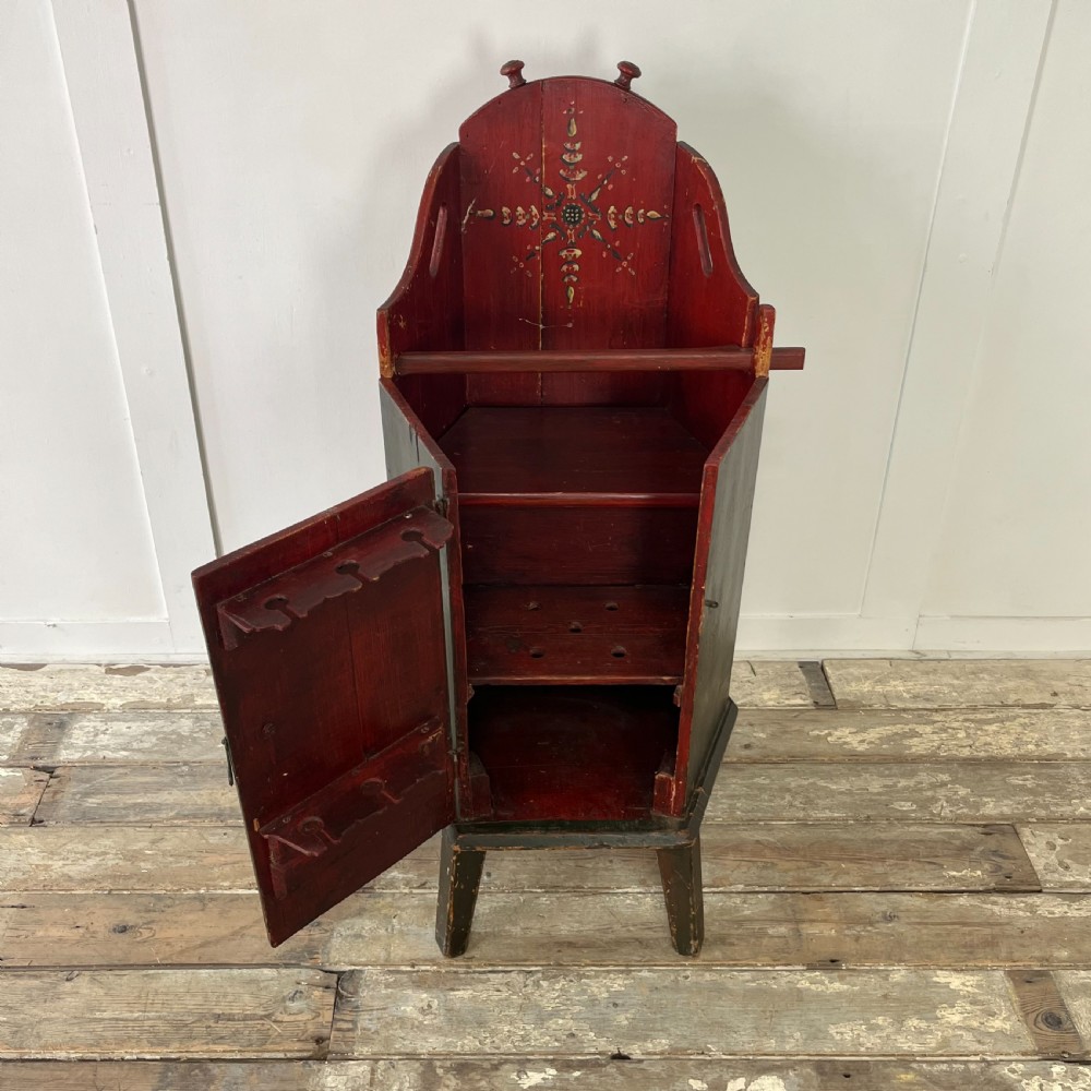 A 19th-century European folk art childs high chair featuring a dark painted enclosed cupboard base and a crimson shaped backrest decorated with hand-painted floral motifs. View VII
