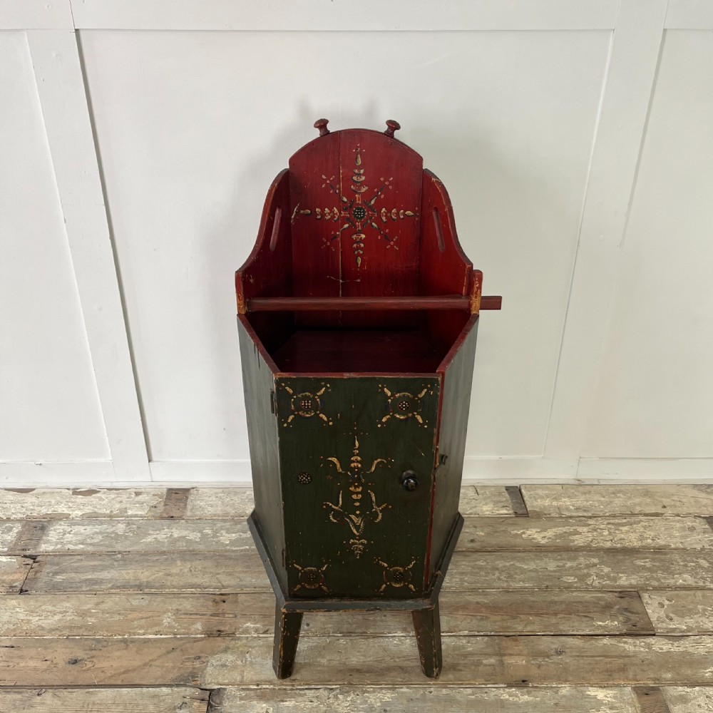 A 19th-century European folk art childs high chair featuring a dark painted enclosed cupboard base and a crimson shaped backrest decorated with hand-painted floral motifs. View IX
