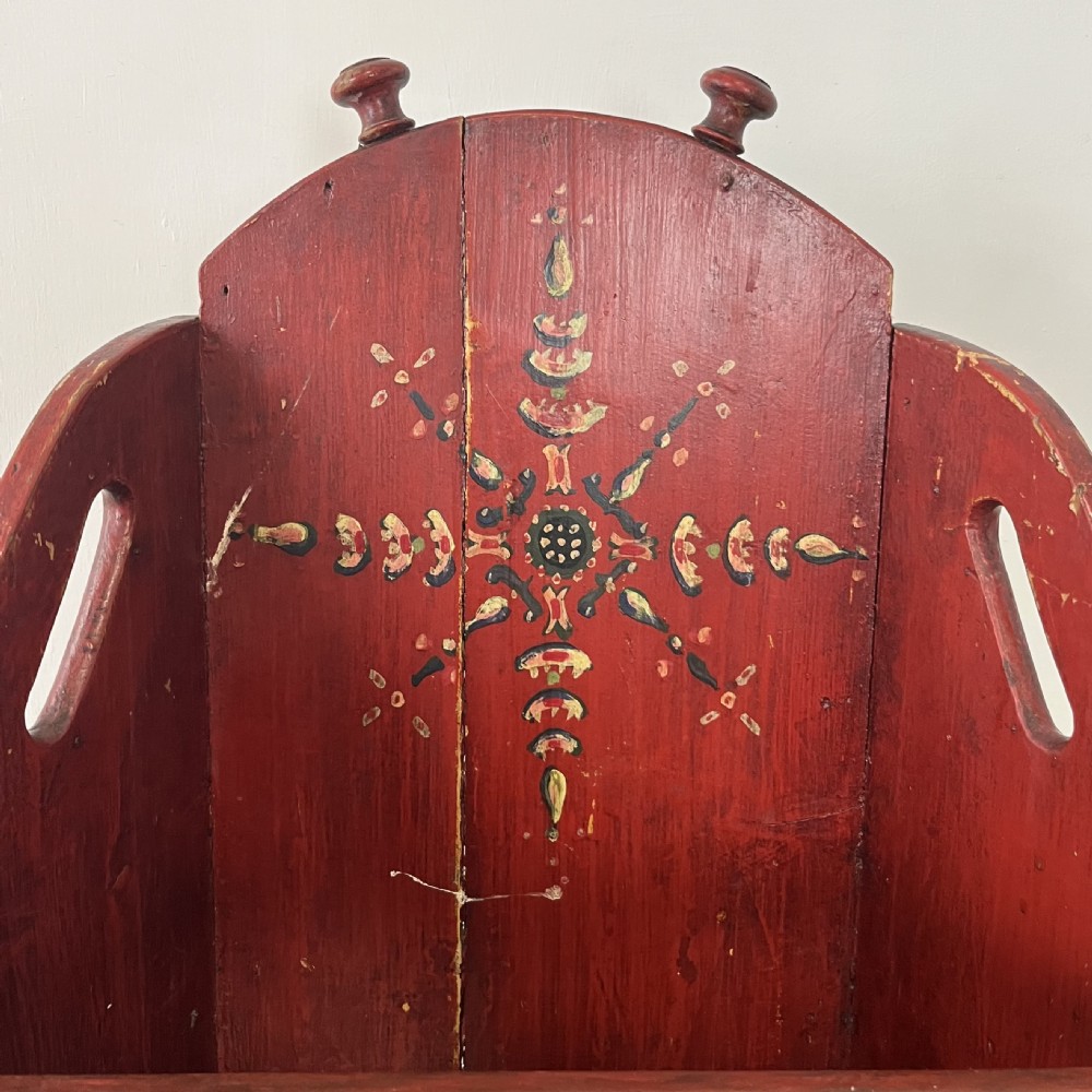A 19th-century European folk art childs high chair featuring a dark painted enclosed cupboard base and a crimson shaped backrest decorated with hand-painted floral motifs. View XIII