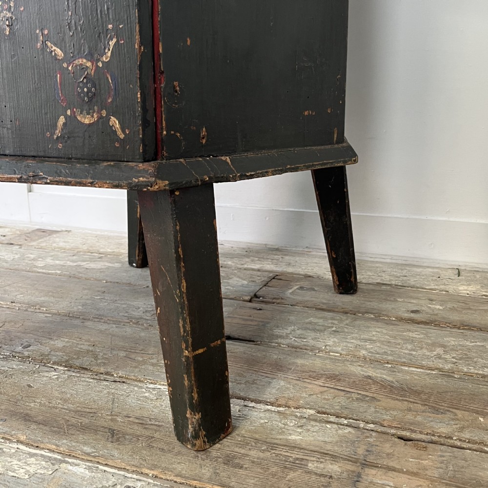 A 19th-century European folk art childs high chair featuring a dark painted enclosed cupboard base and a crimson shaped backrest decorated with hand-painted floral motifs. View XVII
