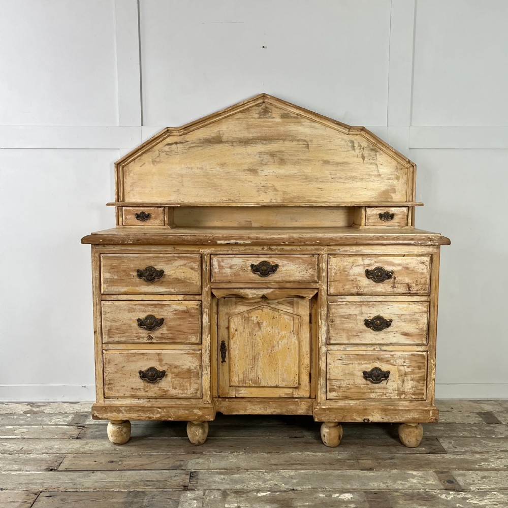 Victorian painted pine dresser with a shaped architectural backboard, multiple drawers, central cupboard, and bun feet in a distressed finish.