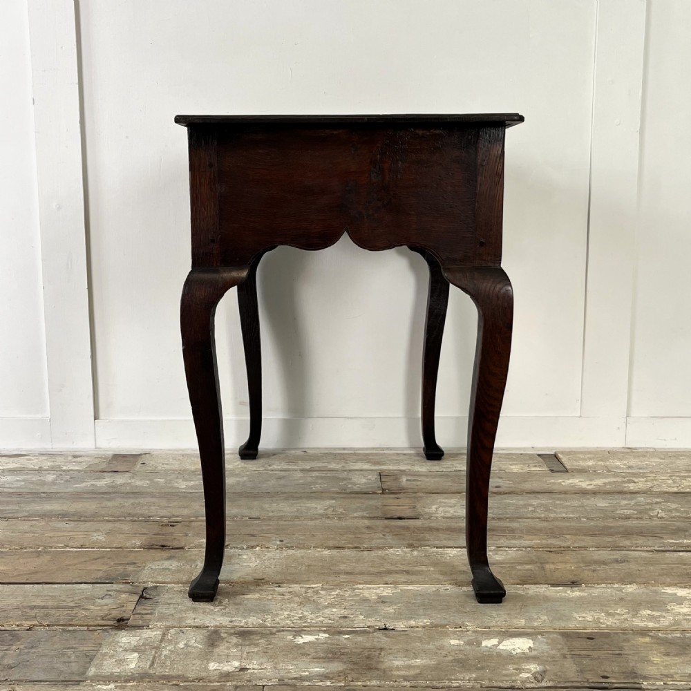 An early 18th-century dark oak lowboy table featuring three drawers, a scalloped apron, and four cabriole legs. View XIV