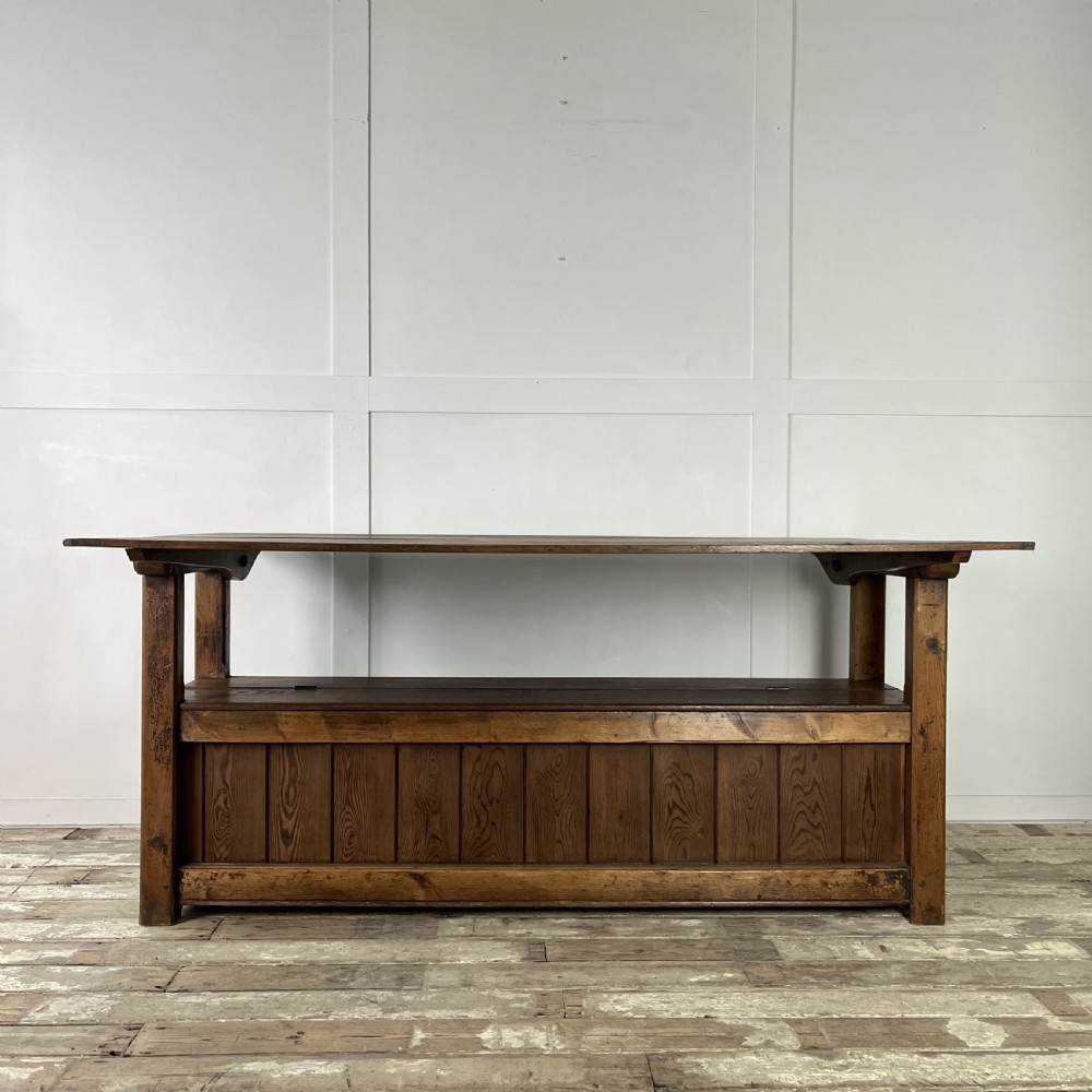 A dark stained Victorian pine monks bench featuring a tall planked backrest, flat wooden armrests, and a vertical panelled base. View II