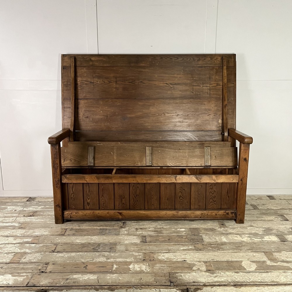A dark stained Victorian pine monks bench featuring a tall planked backrest, flat wooden armrests, and a vertical panelled base. View III
