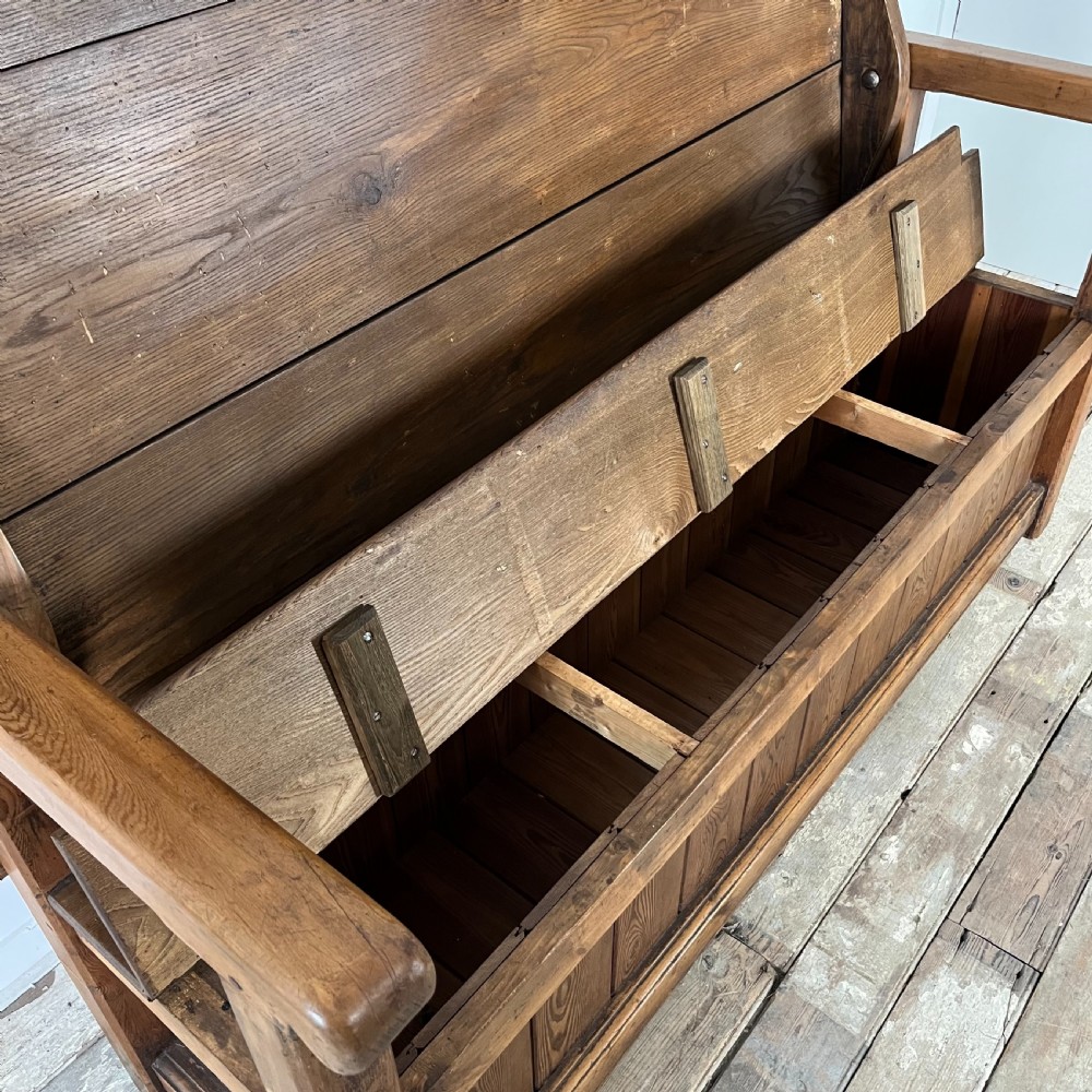 A dark stained Victorian pine monks bench featuring a tall planked backrest, flat wooden armrests, and a vertical panelled base. View V