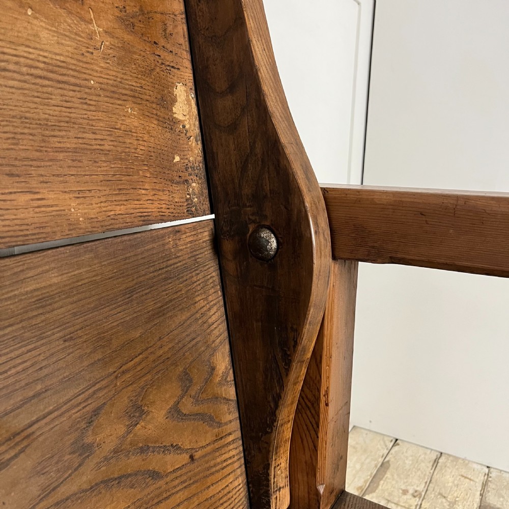 A dark stained Victorian pine monks bench featuring a tall planked backrest, flat wooden armrests, and a vertical panelled base. View VIII