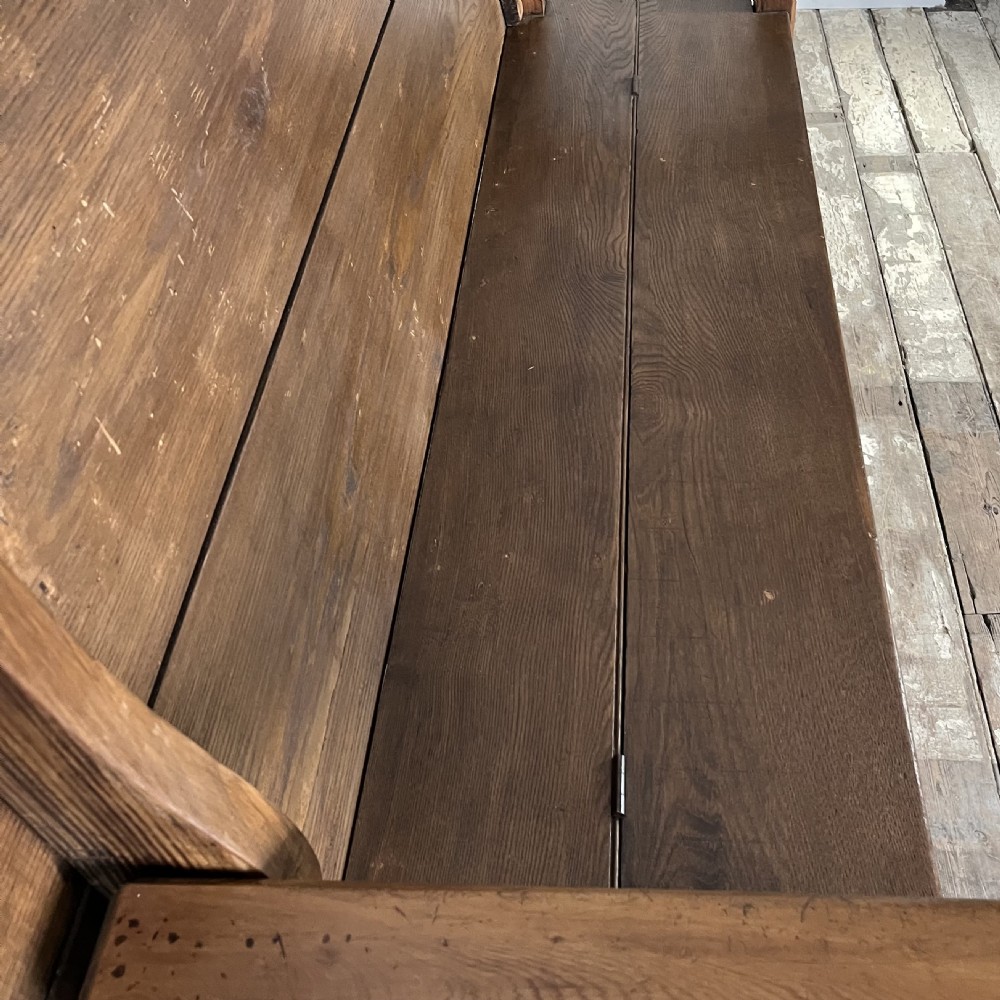 A dark stained Victorian pine monks bench featuring a tall planked backrest, flat wooden armrests, and a vertical panelled base. View X