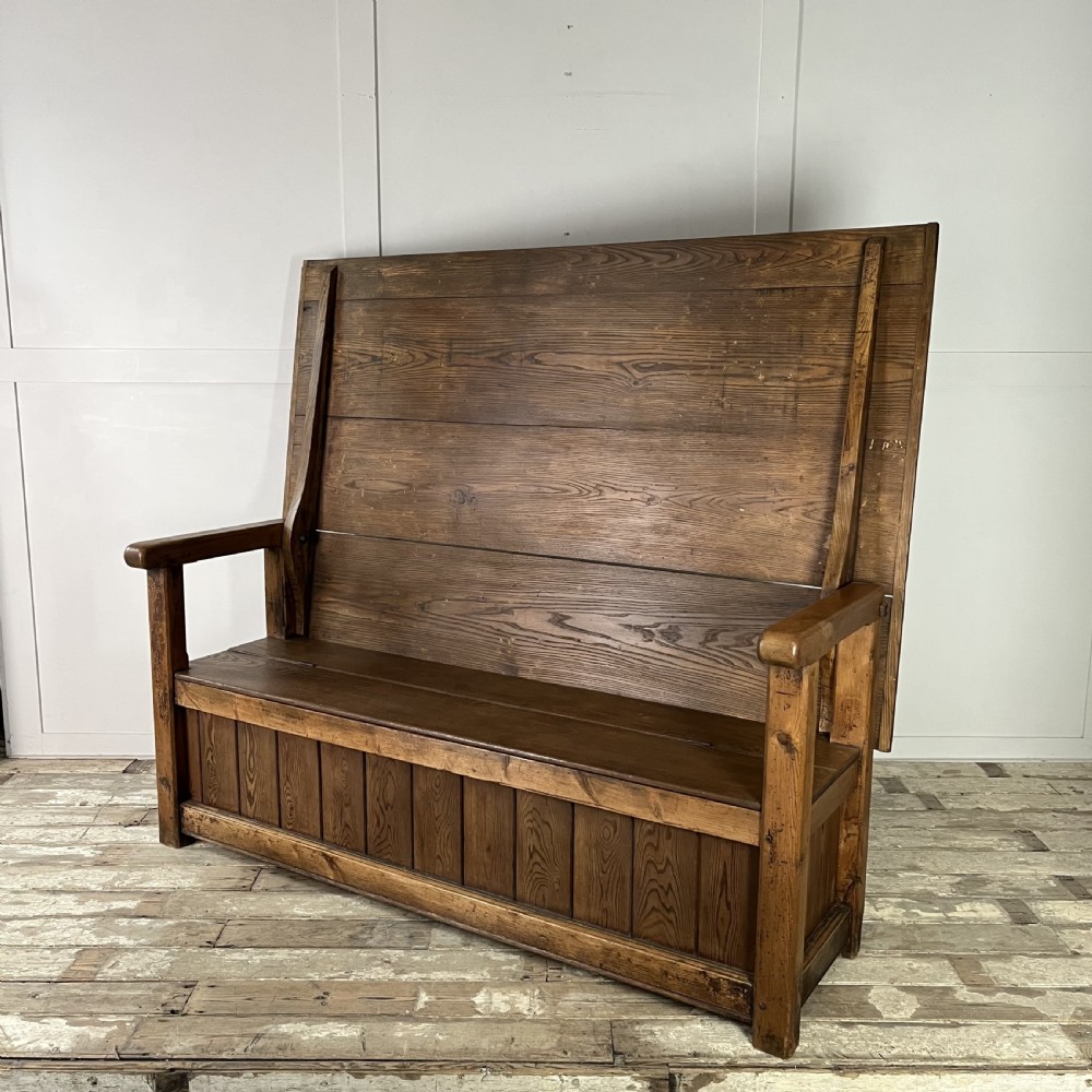 A dark stained Victorian pine monks bench featuring a tall planked backrest, flat wooden armrests, and a vertical panelled base. View XI