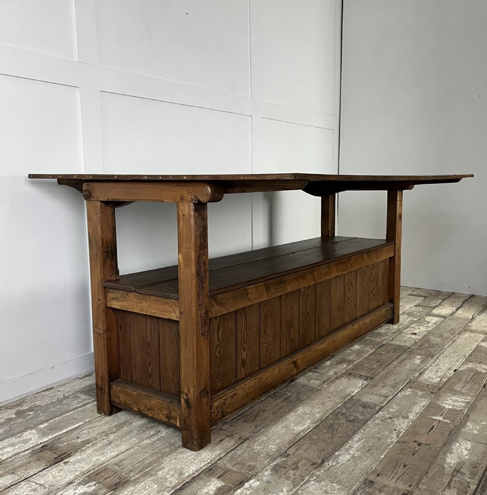 A dark stained Victorian pine monks bench featuring a tall planked backrest, flat wooden armrests, and a vertical panelled base. View XII