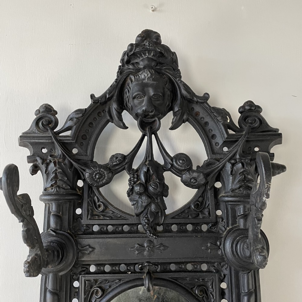 A tall black cast iron Victorian hall stand featuring an integrated central mirror, branching coat hooks, scrollwork tracery, and an umbrella drip tray at the base. View III