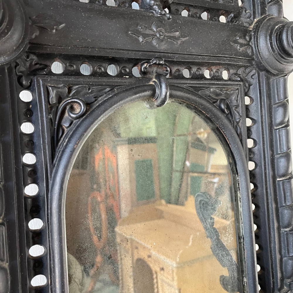 A tall black cast iron Victorian hall stand featuring an integrated central mirror, branching coat hooks, scrollwork tracery, and an umbrella drip tray at the base. View V